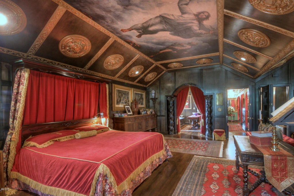 Expansive master bedroom with red and gold furniture and carpeting and sloped roof