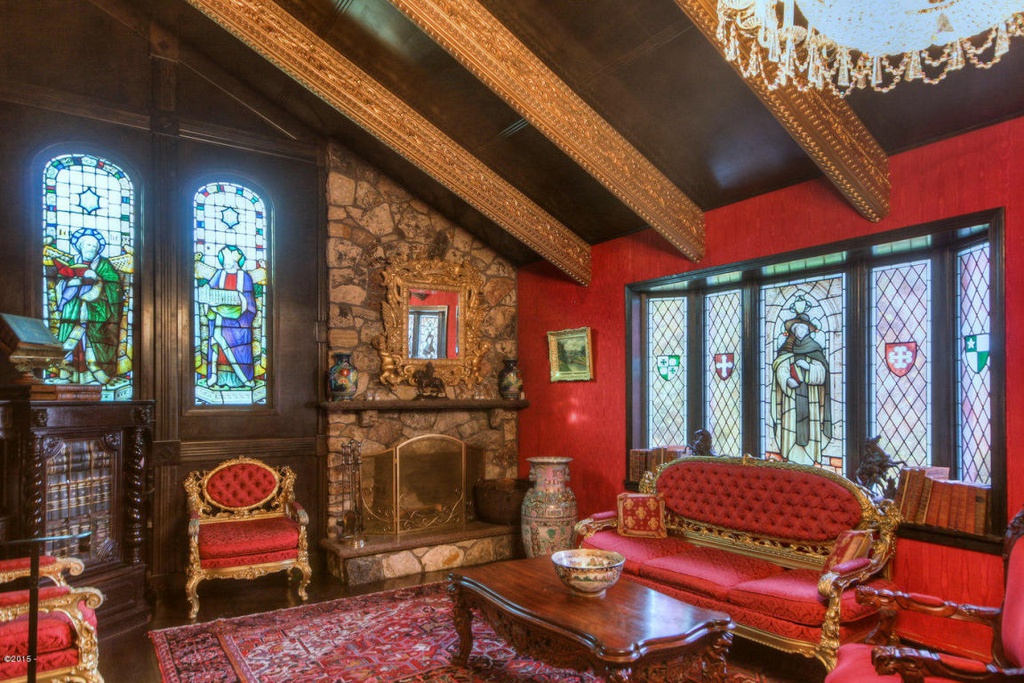A slanted living room roof with stone fireplace, stained-glass windows and plush red and gold furniture