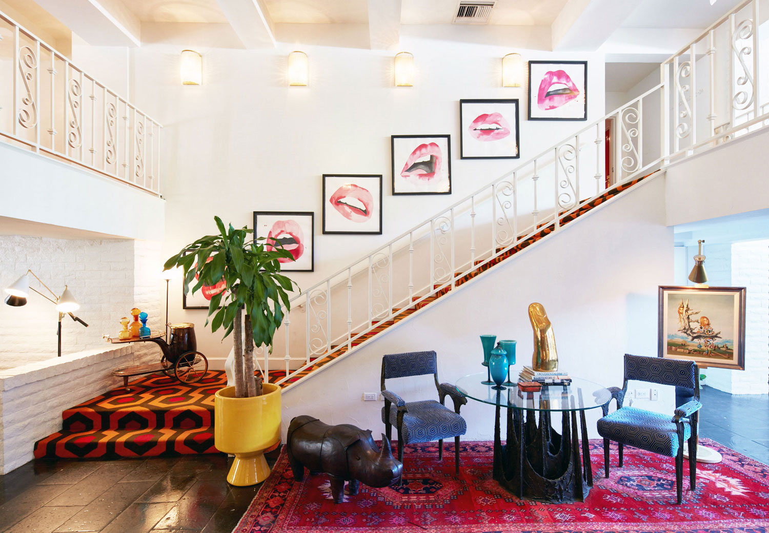 staircase with geometric carpet, framed lip artwork along wall, sitting area with leather rhino