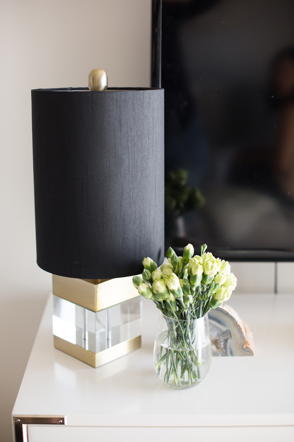 Black, gold and lucite lamp on dresser with small vase of carnations