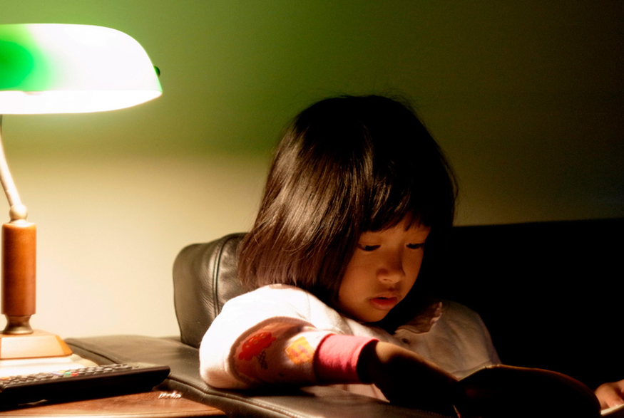 Girl reading next to lamp on side table