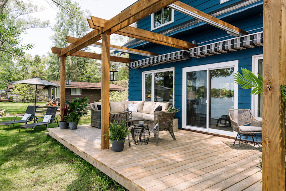 blue house exterior with wooden pergola, striped retractable awning and wood deck