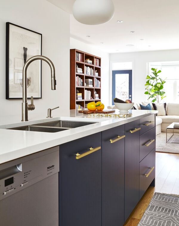 blue kitchen island with brass pulls and white top with stainless steel Miele dishwasher in foreground, living room in distance
