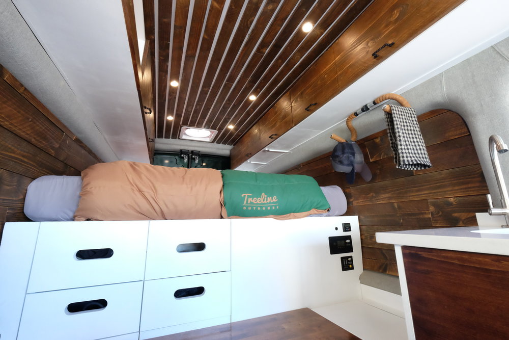 wood and white camper van interior with storage under platform bed