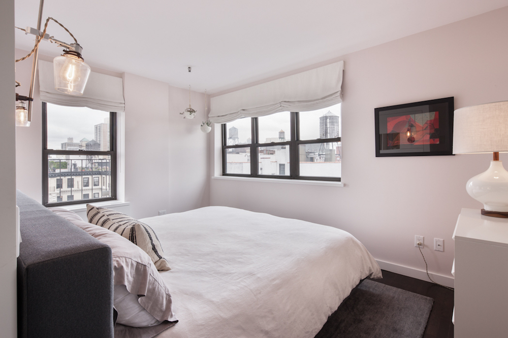 white bed in white bedroom with windows facing city