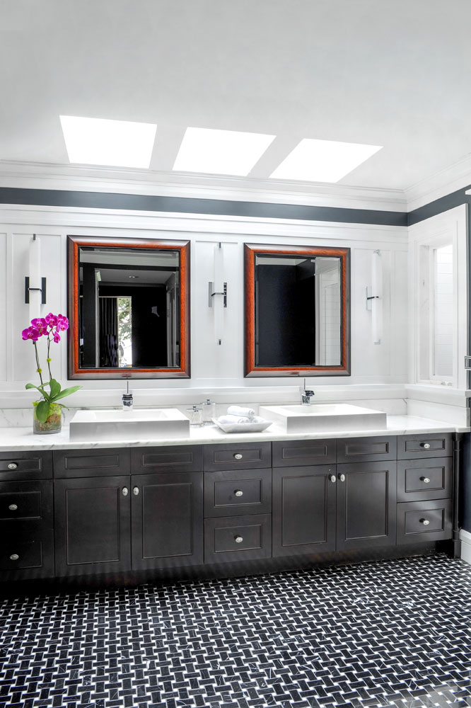 skylit bathroom with grey vanity, double sinks and black and white woven marble floor