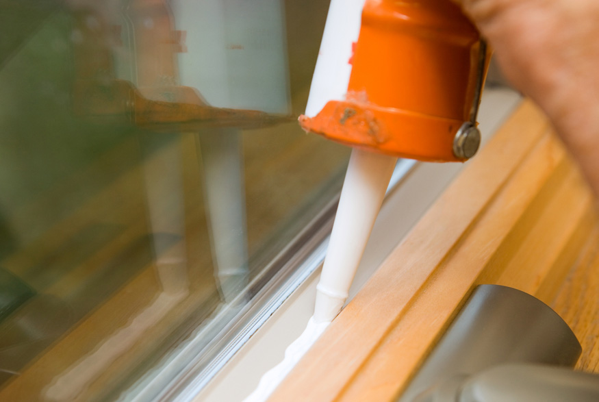 An orange caulking tool being used on a window frame