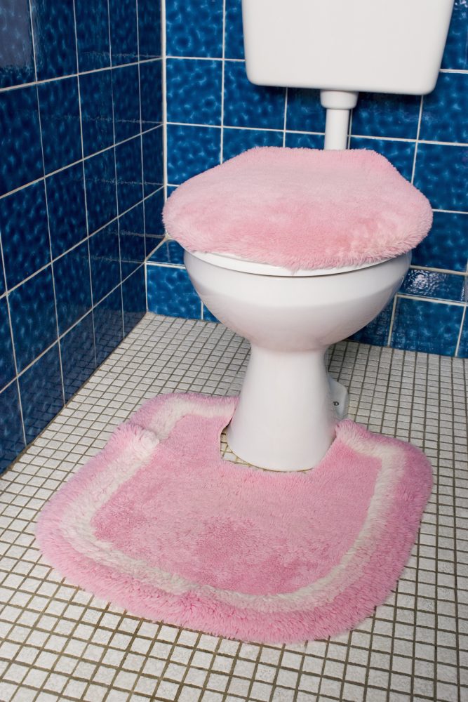 A toilet surrounded by a pink shag-rug and covered by a pink toilet seat cover