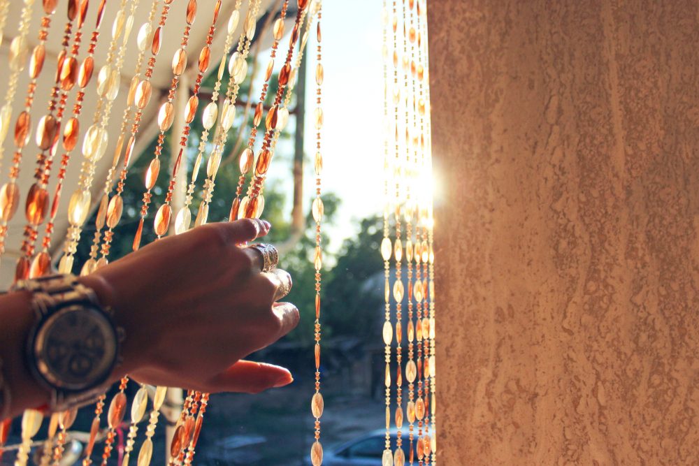 A hand brushing aside a beaded curtain