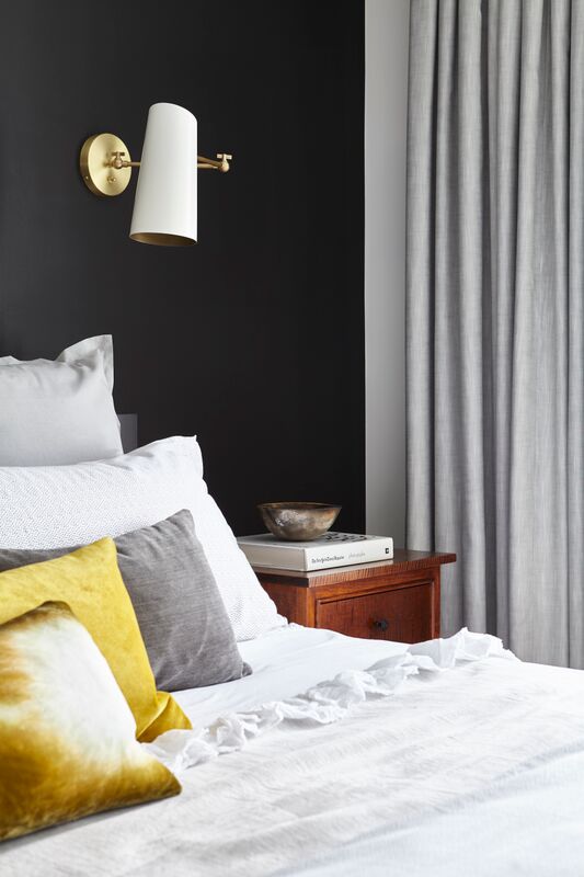 closeup of white and brass sconce on black focal wall behind bed with grey and mustard cushions