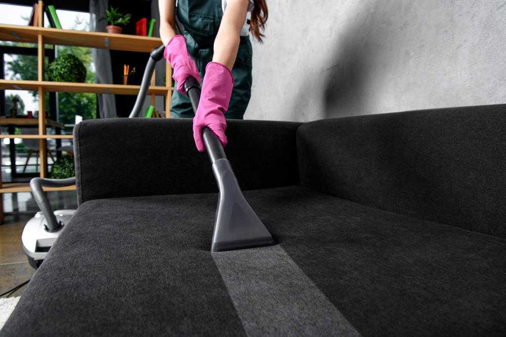 A woman with gloved hands vacuuming a couch