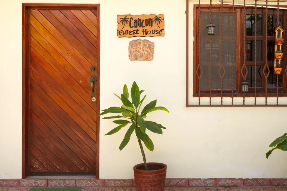 Guest house in Cancun with thick wooden door, window grates and a potted plant on the front porch
