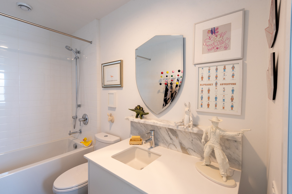 white bathroom with playful decor objects and shield-shaped mirror