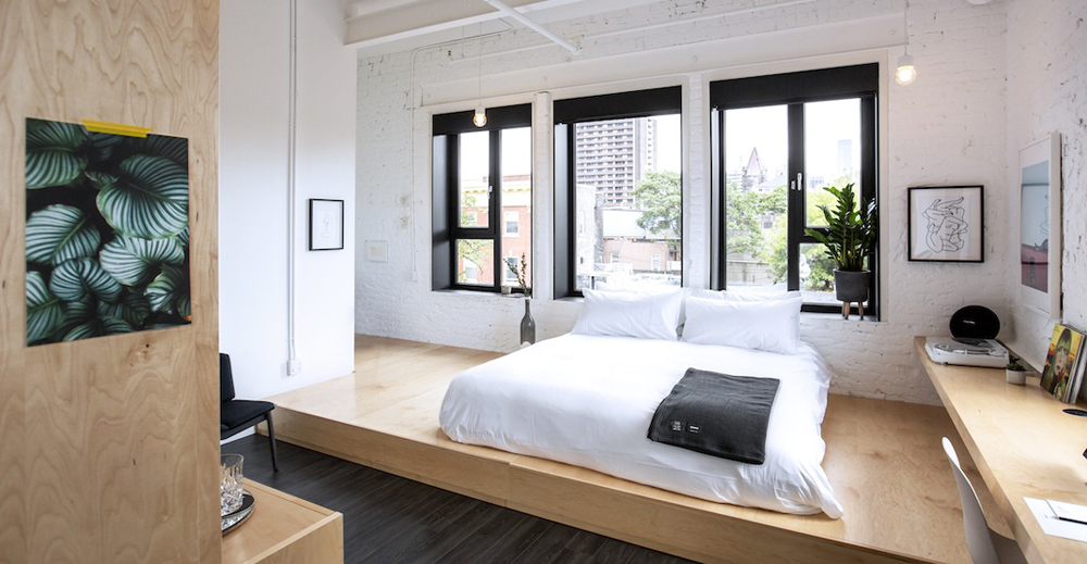 white loft bedroom with plywood platform bed and black windows