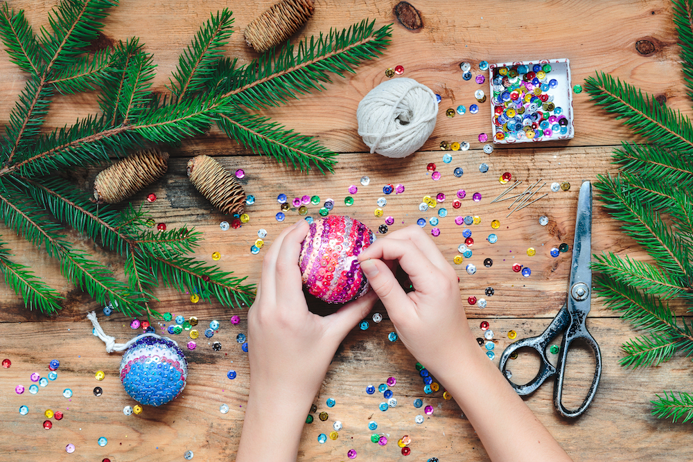 Cropped hands making colourful sequinned Christmas decoration on wood table