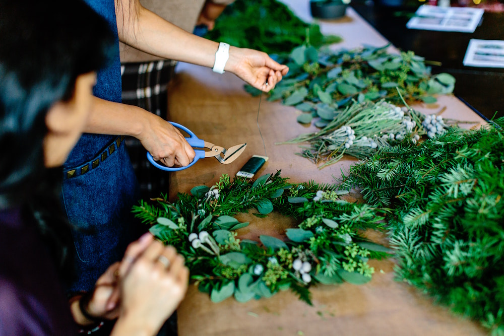 people making their own green wreaths on wood table
