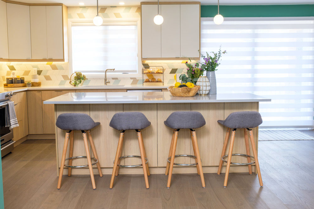 A sleek renovated kitchen with an island and four chairs pulled up to it