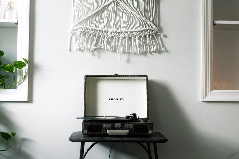 A record player situated beneath a macrame wall hanging