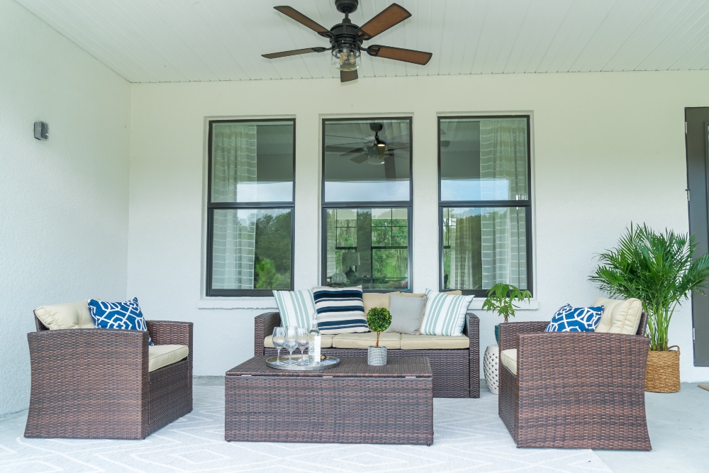 A back porch area with a brown wicker sofa and two chairs arranged in a U shape around a coffee table.