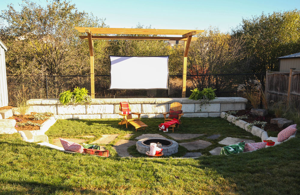 Backyard movie theatre with screen, fire pit and seating with an assortment of pillows