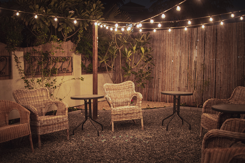 Nighttime shot of a yard with wicker chairs and strings of fairy lights all fenced in by a bamboo screening fence.