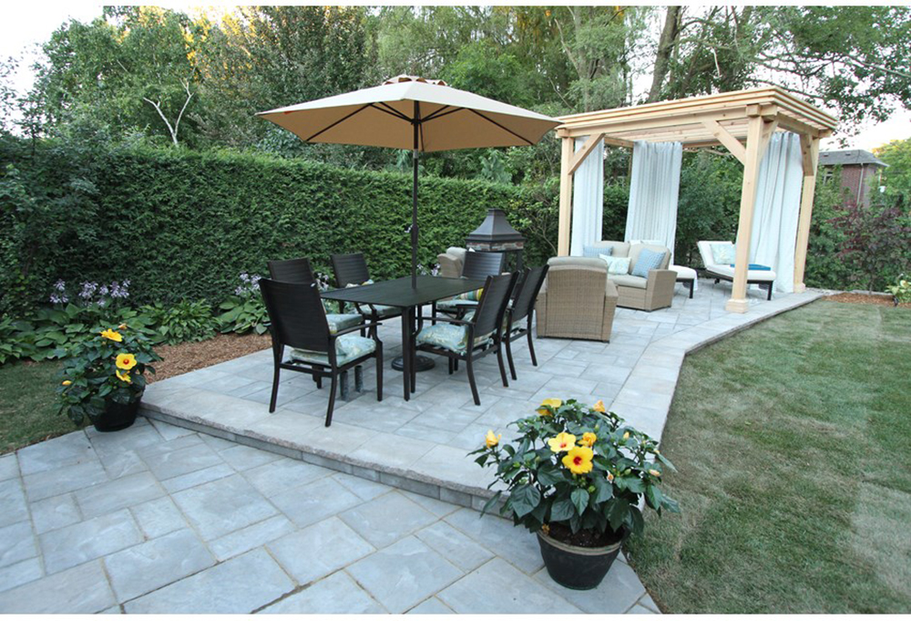 A backyard patio with a dining set, conversation set and pergola. A hedge fences in the patio area.