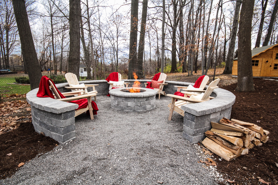 grey brick fire pit with wood chairs and red accents in backyard