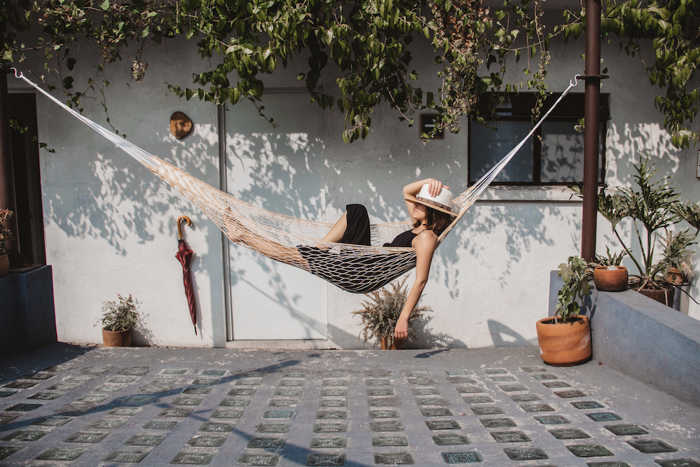 woman laying on woven hammock in front of white exterior wall
