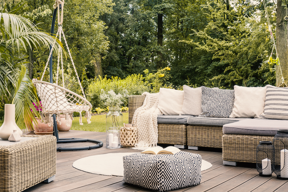 Book on a black and white pouf in the middle of a bright terrace with a rattan corner sofa, hanging chair and round rug