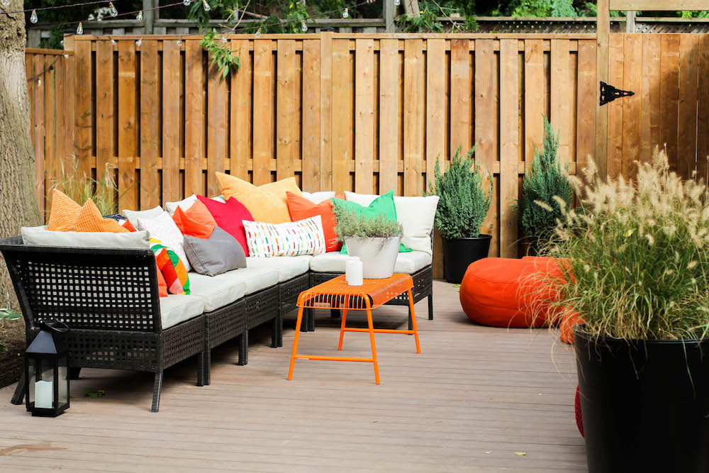 black outdoor seating with colourful pillows in front of wooded fence