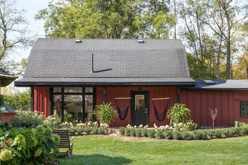 red converted barn with green landscaping and two black hanging chairs