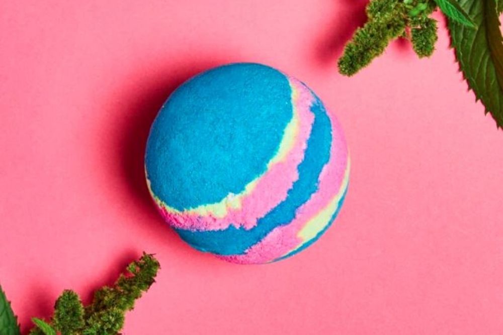 A bright blue, pink and white bath bomb against a bright pink background