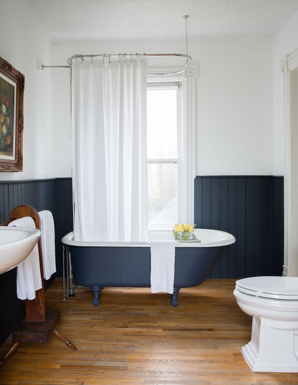 A renovated home with wood flooring, midnight blue walls and a clawfoot tub