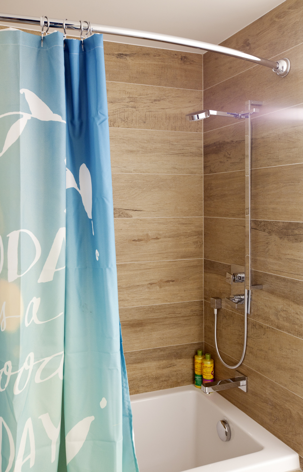 An outdoorsy bathroom renovation with wood-inspired tiles paired with summery shower curtains
