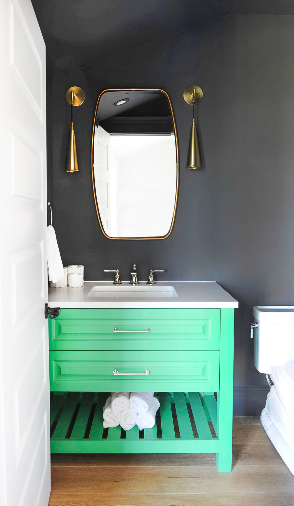 A small bathroom with dark grey walls offset by bright pastel green cabinetry