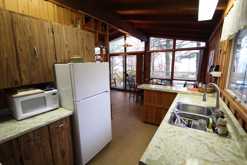 Kitchen in an outdated cottage with beige countertops and wood paneling