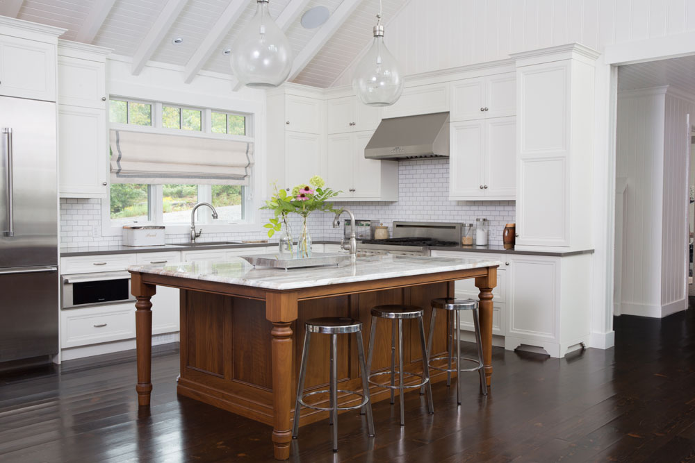 white kitchen with dark wood floors and marble top island in medium tone wood with three steel stools