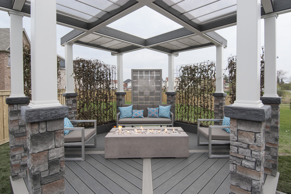 Outdoor pergola outfitted with a modern fireplace, hefty stone pillars and stylish furniture.