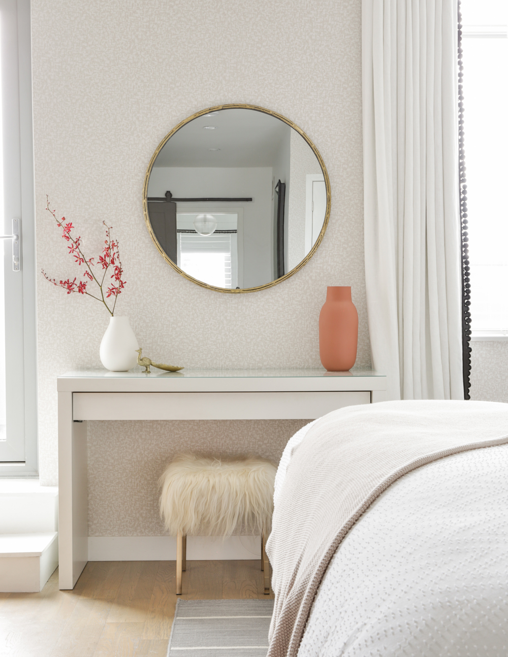 A circular mirror above a small desk in a renovated bedroom with a soothing colour palette