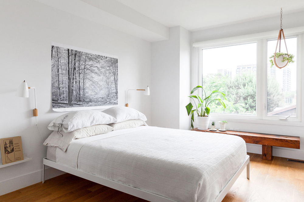 A minimalist white bedroom with very little furniture aside from a bench with potted plants