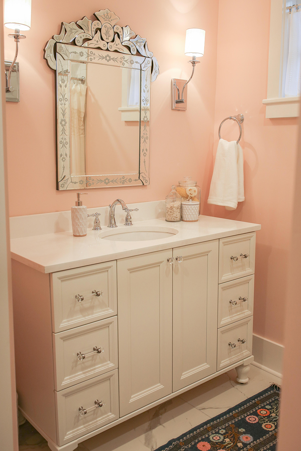 A blush pink master bathroom with porcelain tile that resembles marble and a decorative mirror