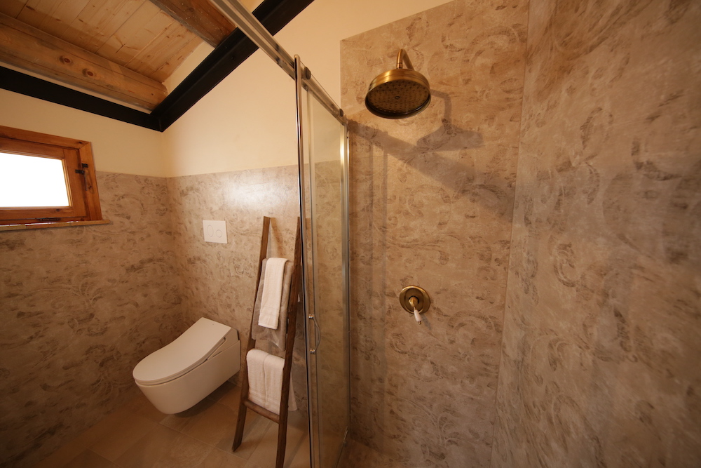 grey bathroom with stone tile, shower and white toilet