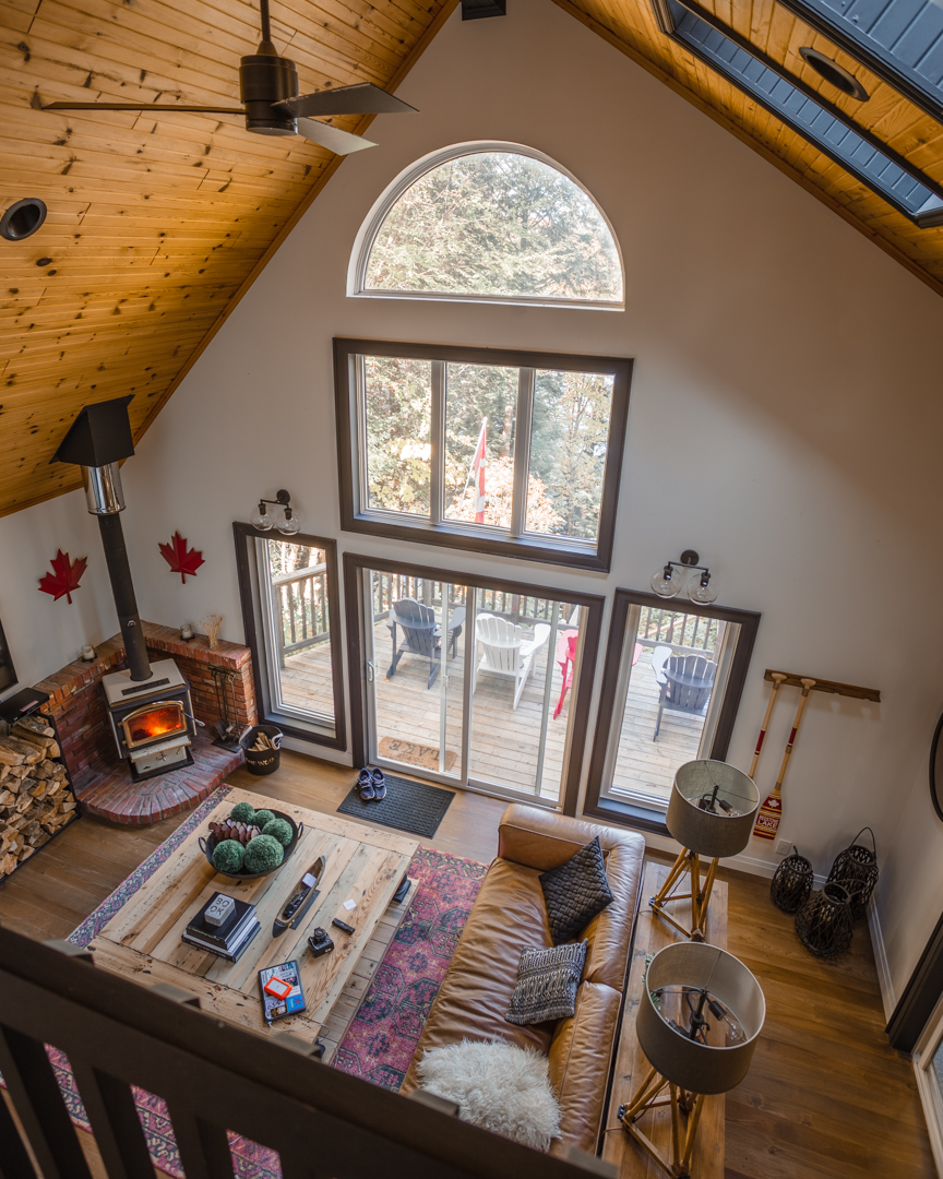aerial view into cottage living room, double ceiling, wood stove in corner with two red maple leaves on wall by stove