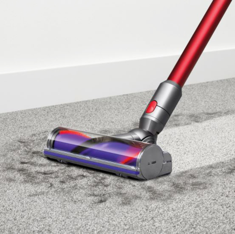 A closeup of the iron red Dyson vacuum cleaning a grey carpet