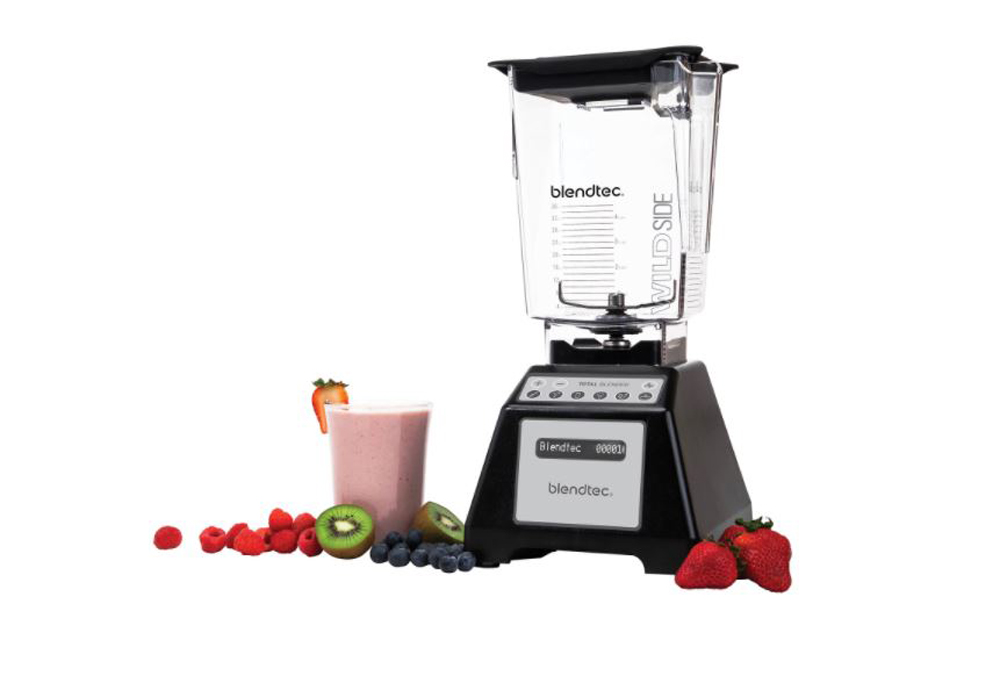 An empty black blender surrounded by various fruits and a tall glass filled with a purple smoothie