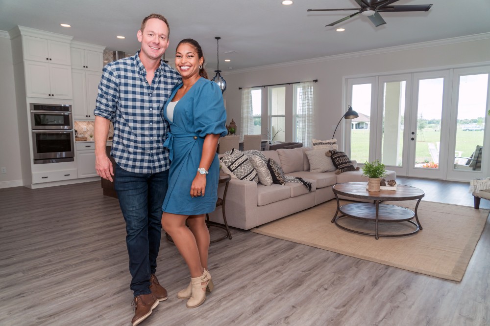 100 Day Dream Home's Brian and Mika Kleinschmidt standing in the great room of clients' Betin and Yara's new home. The living, dining and kitchen areas are behind them.