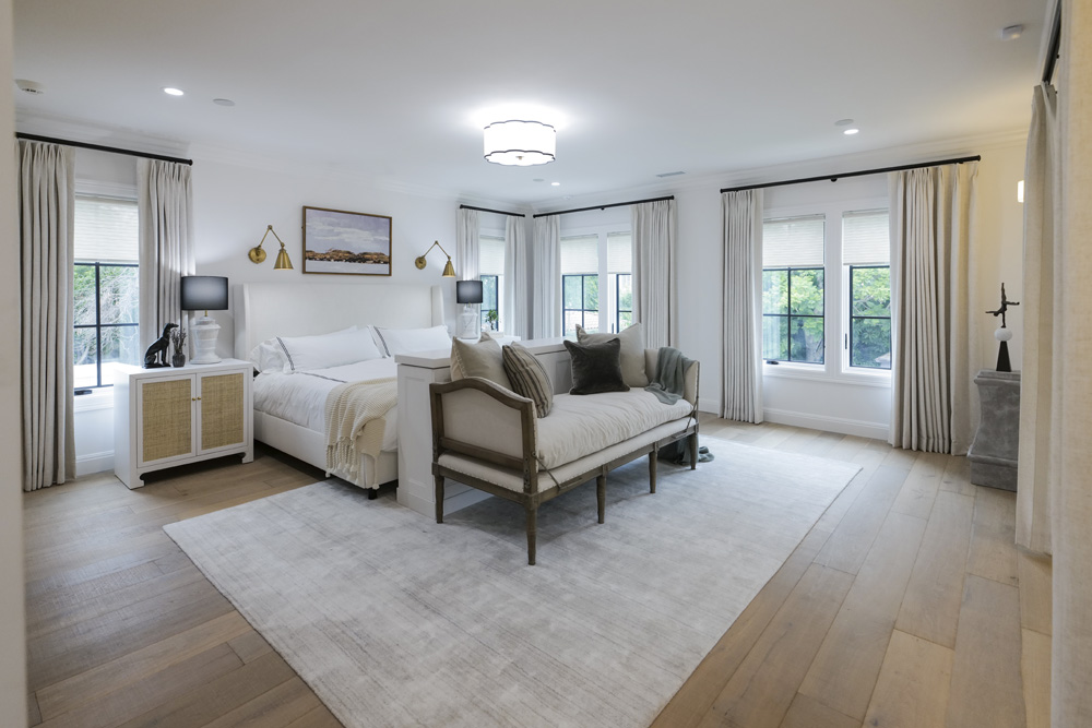 A spacious main bedroom in soothing colour palette with tons of natural light, area rug and a seating area