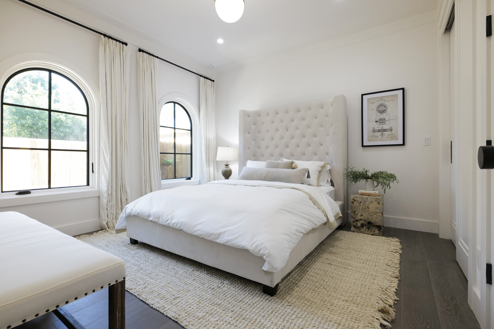 A white renovated guest house bedroom with an oversized headboard and area rug