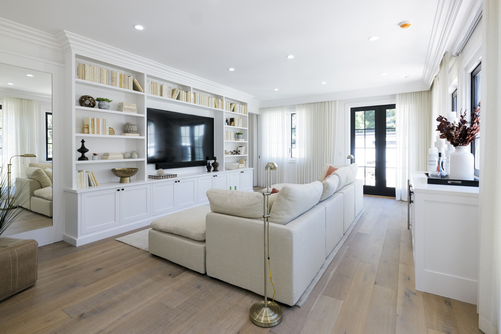 A white monochromatic media room in a renovated guest house with oversized TV and plenty of seating