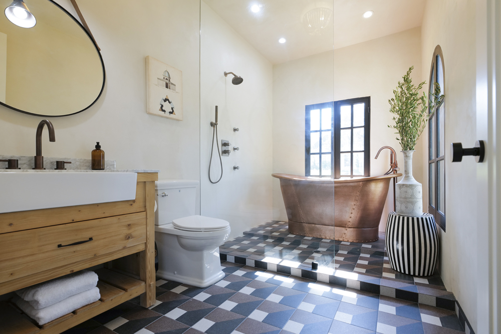 A renovate bathroom with wood vanity, checkered tile floors and a bronze stand-alone tub